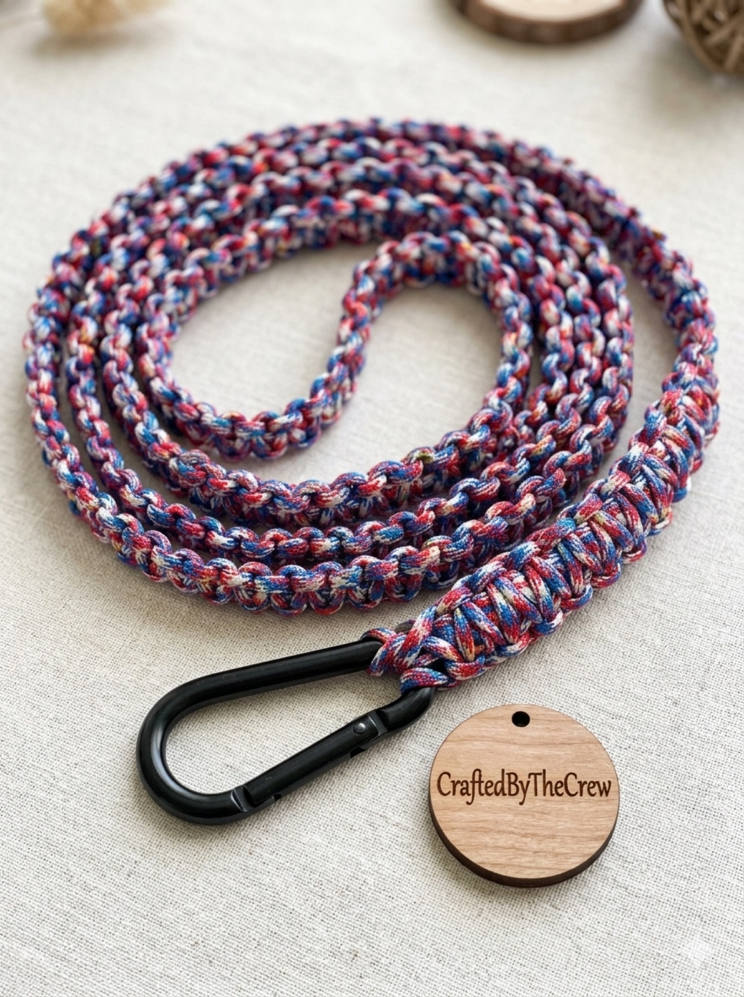 Red white and blue paracord leash with a black carabiner and a wooden Crew tag